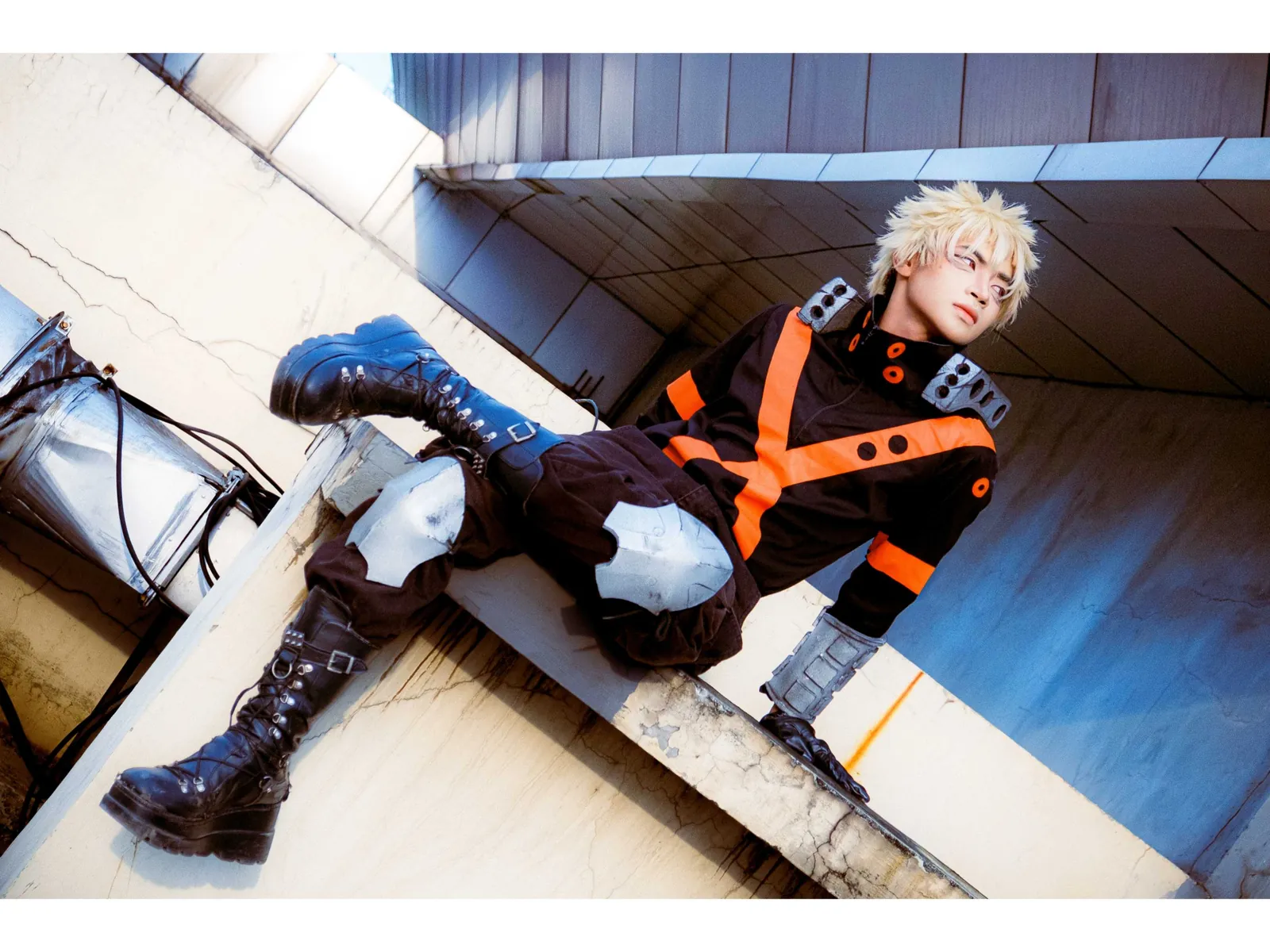 Bakugo cosplay in a black and orange costume posed on a concrete ledge