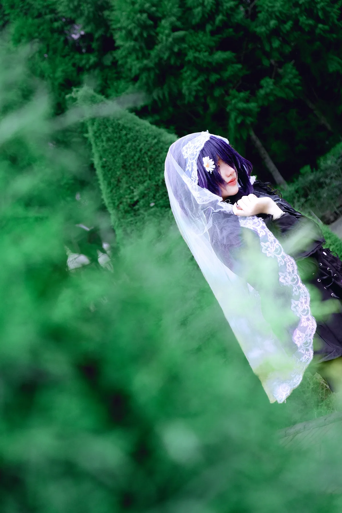Reze cosplay portrait with a white lace veil among green foliage