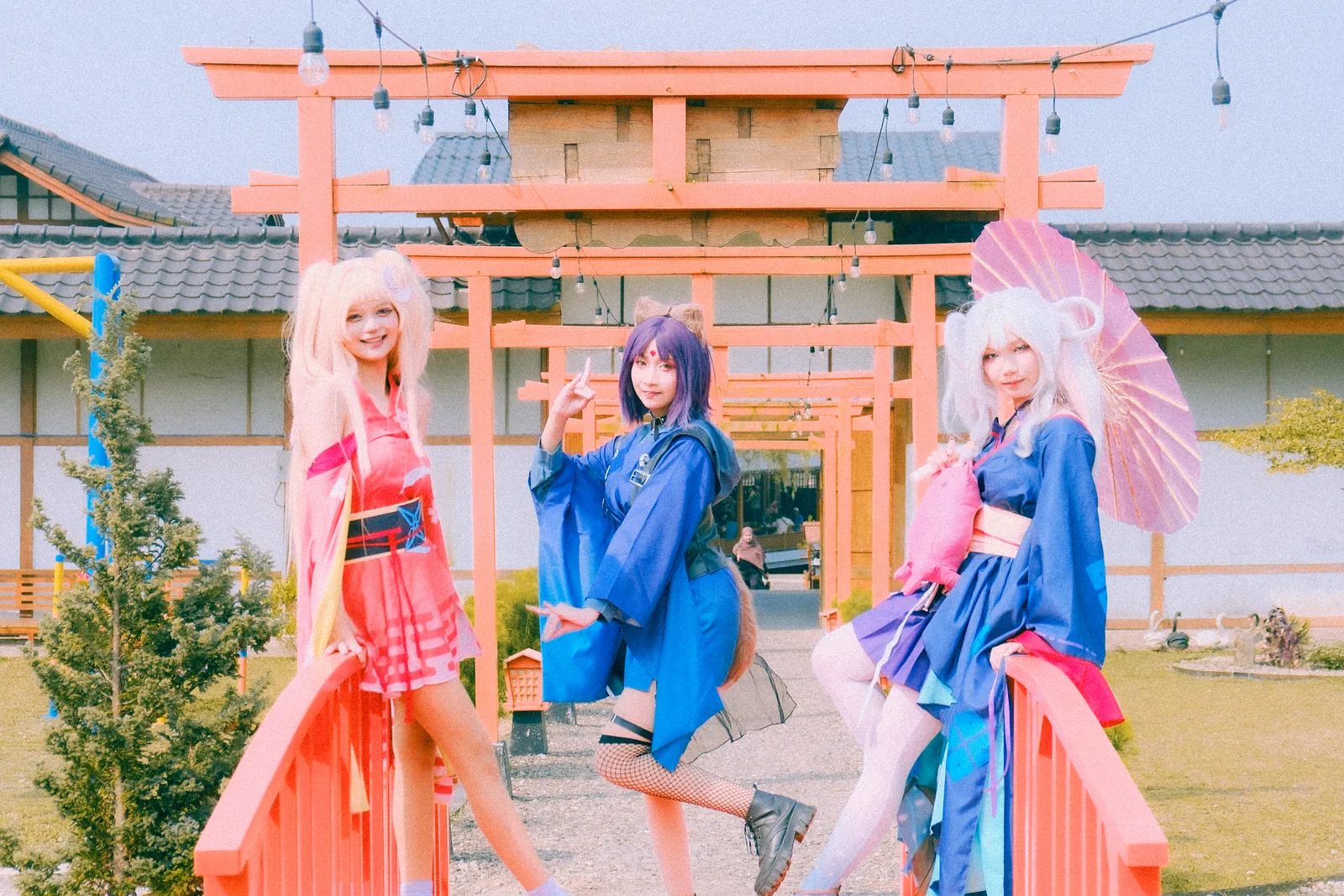 Three cosplayers posing together in front of red torii gates